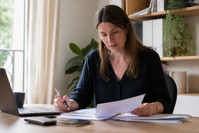 Une femme française examine des documents et prend des notes dans son bureau à domicile, en préparant son projet de rénovation.