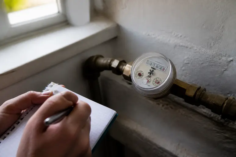 Un compteur d'eau est observé attentivement, une personne relève le chiffre pour détecter une éventuelle fuite dans l'installation domestique.
