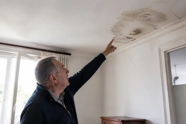 Un propriétaire français examine une tache d'humidité au plafond, signe d'une fuite provenant des étages supérieurs.