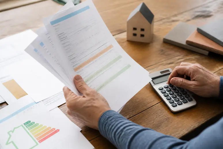 Mains d'un propriétaire français tenant des documents officiels et une calculatrice pour estimer le montant des aides à l'isolation en 2026.