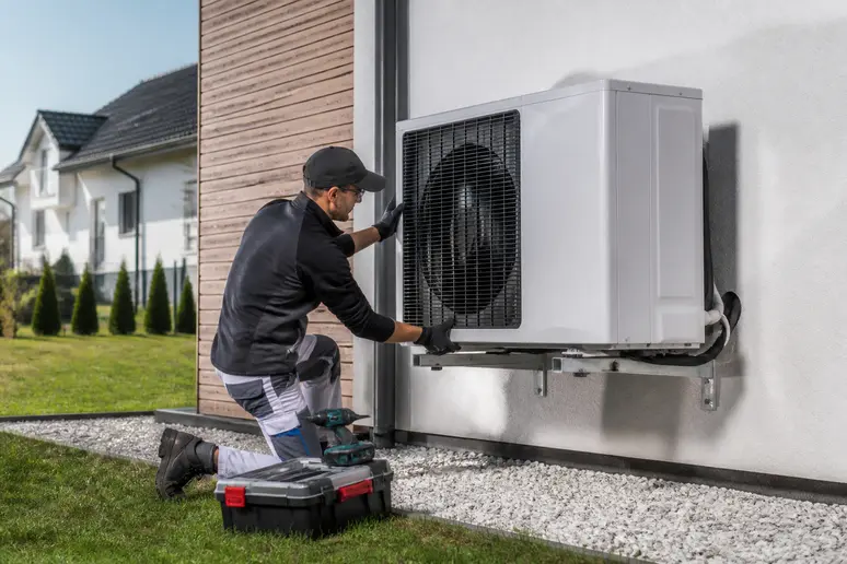 Un plombier installe une pompe à chaleur air-eau sur la façade d'une maison, détaillant le processus technique de l'équipement.