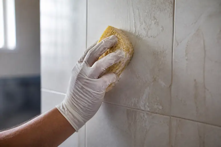 Préparation méticuleuse d'un mur de salle de bain par une main gantée, nettoyage avant peinture essentielle pour un résultat durable.