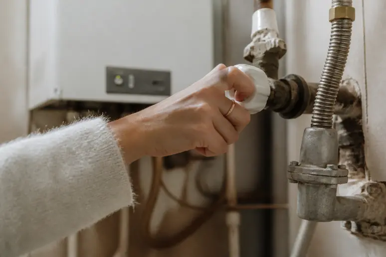 Mains d'une femme actionnant une vanne d'arrivée de gaz sur une chaudiere-atlantic-naia.