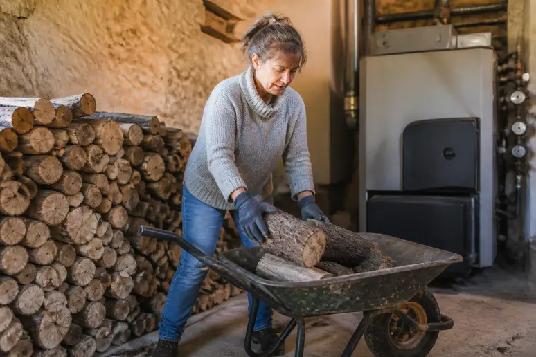 Une femme remplit une brouette de bois sec pour alimenter sa chaudière bois dans une cave aménagée.