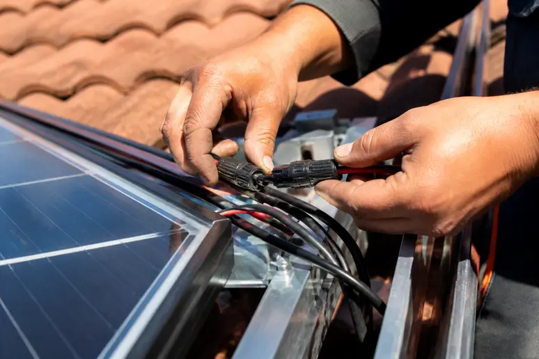 Mains d'un installateur connectant méticuleusement des câbles sur le système de fixation d'un panneau solaire.