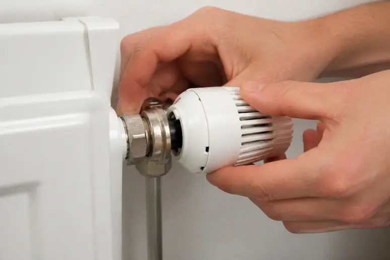 Mains desserrant manuellement la bague de fixation d'une tête de robinet thermostatique bloqué.