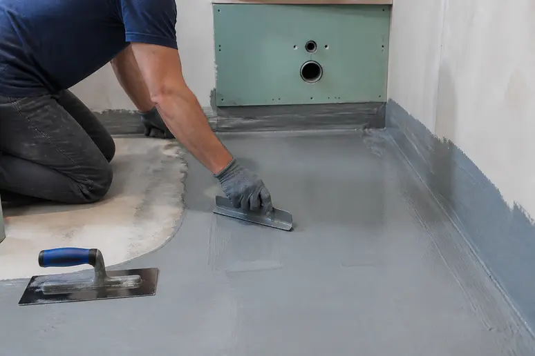 Application méticuleuse d'une membrane d'étanchéité sur le sol d'une salle de bain en rénovation.