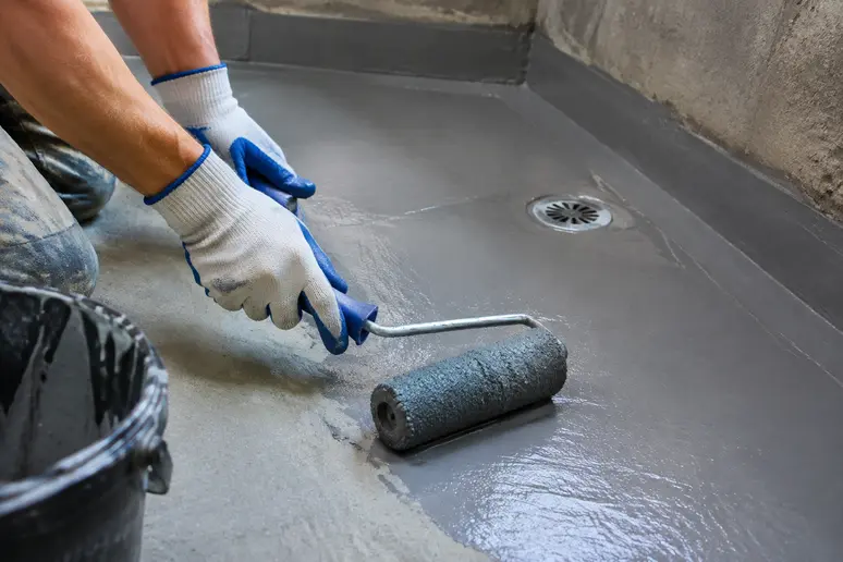 Application minutieuse d'une résine d'étanchéité liquide sur le sol d'une douche à l'italienne avant la pose du carrelage