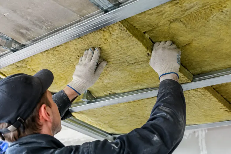 Pose de laine minérale dans l'ossature métallique d'un faux plafond d'appartement