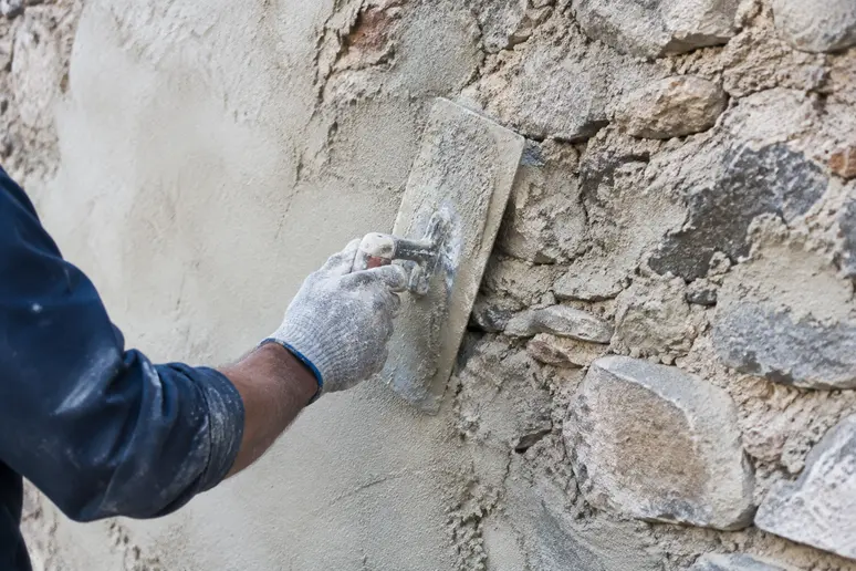 Application manuelle d'un enduit à la chaux sur un mur en pierre ancien