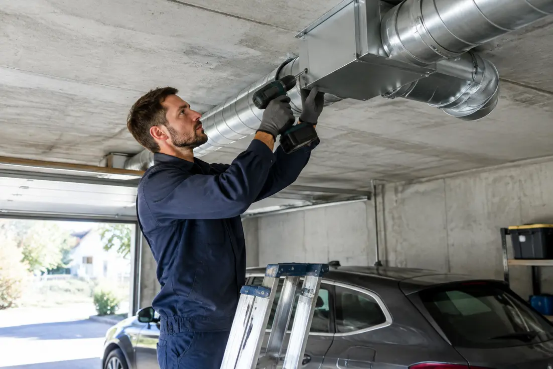 Technicien installant un système de vmc garage au plafond avec une perceuse